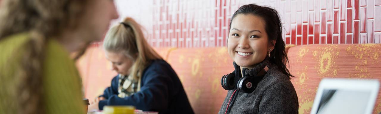 Photo of a female student smiling at the camera with headphones around her neck.
